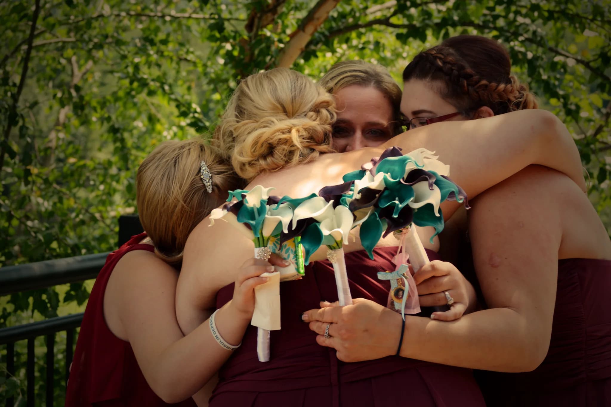 Bridesmaids in maroon dresses hug with teal bouquets on a deck at Moose Hollow Lodge in the Smoky Mountains.