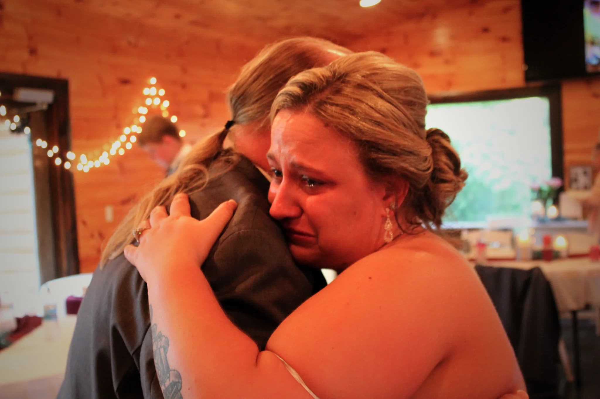 Emotional bride hugging a guest in a rustic wood-paneled event space at Moose Hollow Lodge in Pigeon Forge