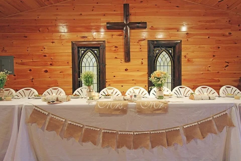 Decorated wedding head table in rustic chapel with wooden cross at Moose Hollow Lodge in Pigeon Forge