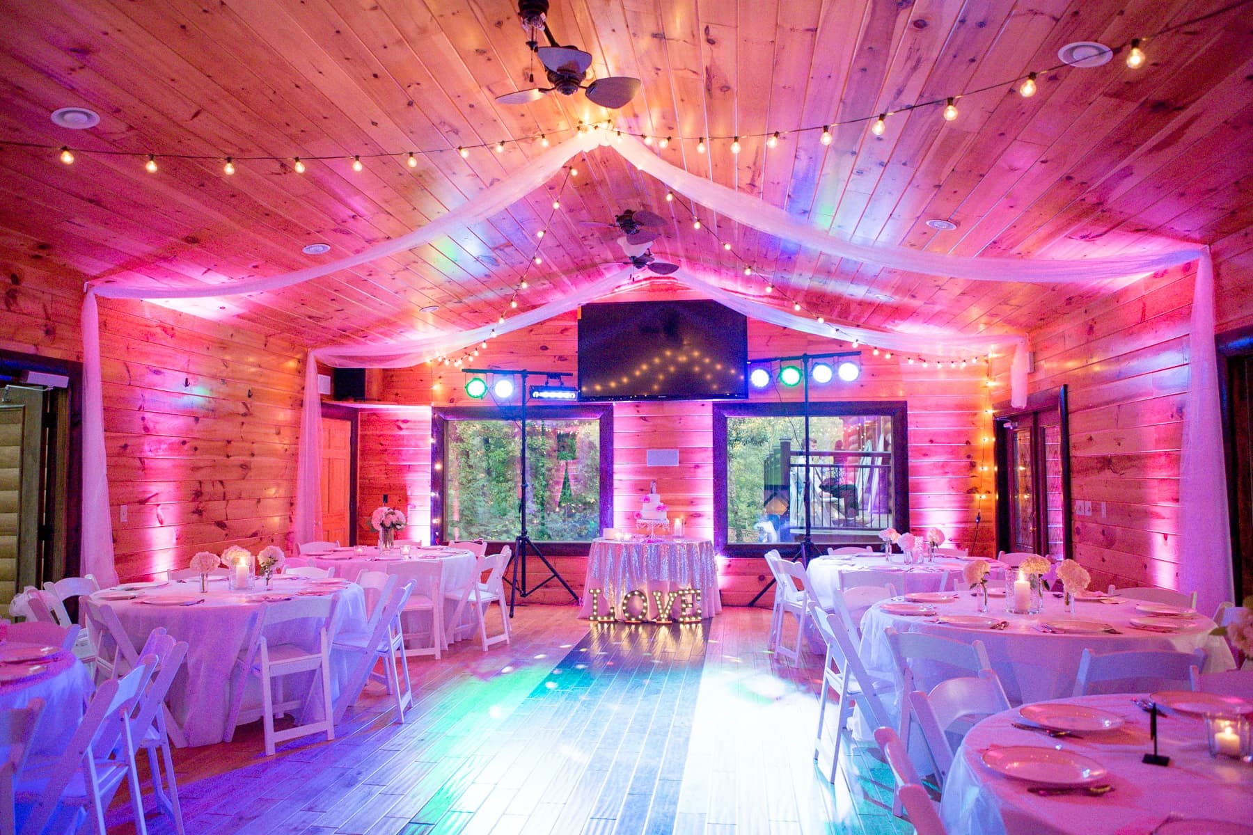 Rustic wedding reception with pink uplighting and string lights at Moose Hollow Lodge in Pigeon Forge