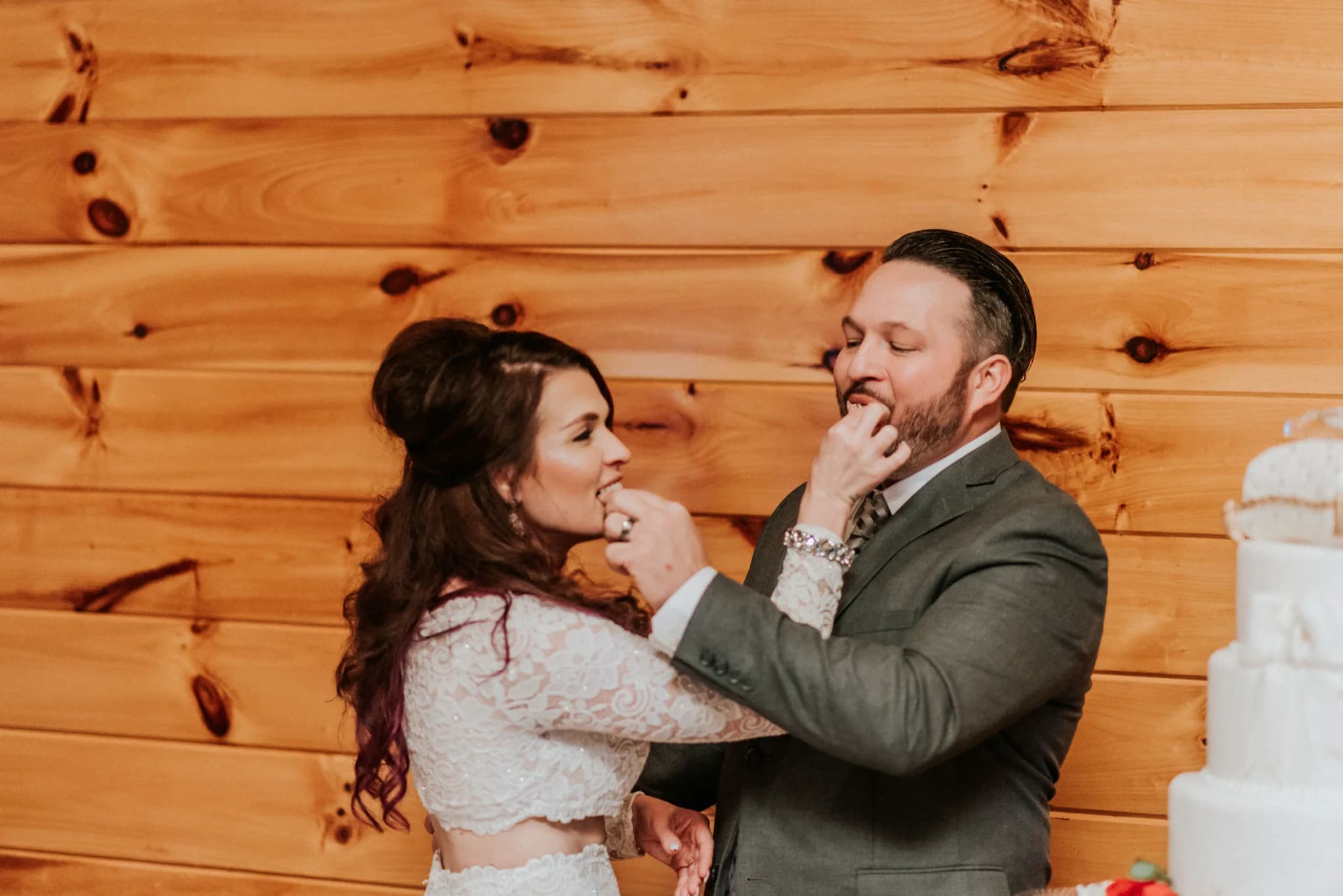 Newlyweds sharing cake against a rustic wood-paneled wall at Moose Hollow Lodge in Pigeon Forge