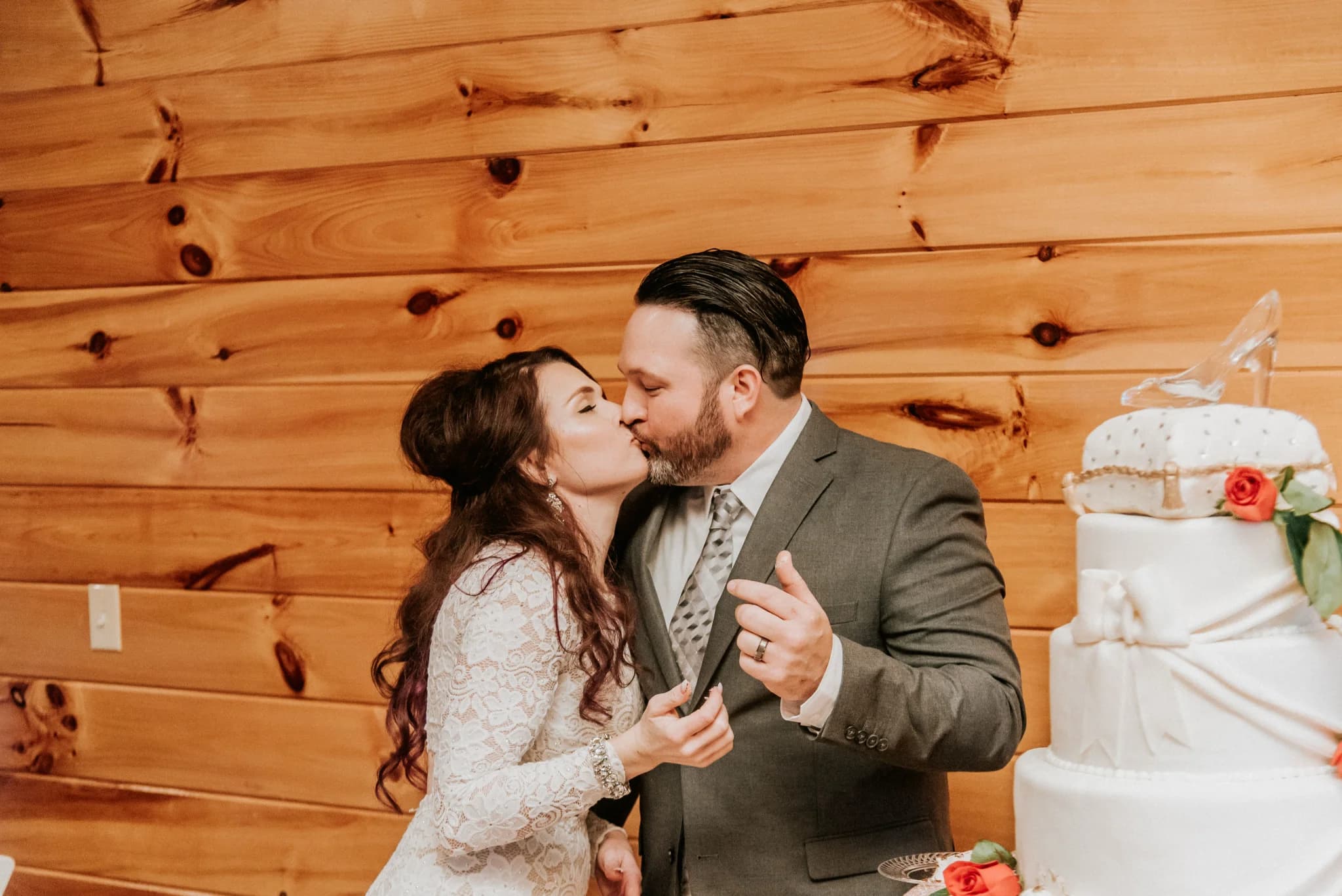 Bride and groom kissing by a wedding cake in a rustic wood-paneled room at Moose Hollow Lodge in Pigeon Forge
