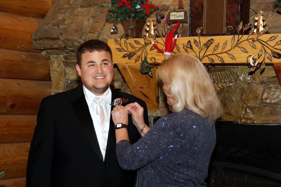 Groom getting boutonniere pinned by stone fireplace in a log cabin at Moose Hollow Lodge in Pigeon Forge