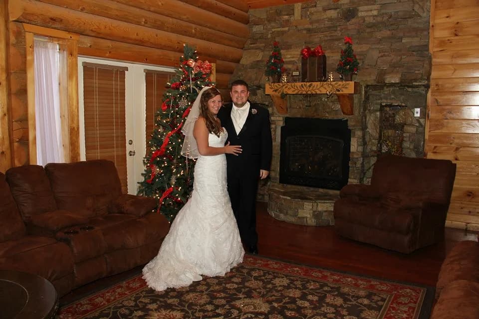 Newlyweds in a rustic living room with stone fireplace and Christmas tree at Moose Hollow Lodge in Pigeon Forge
