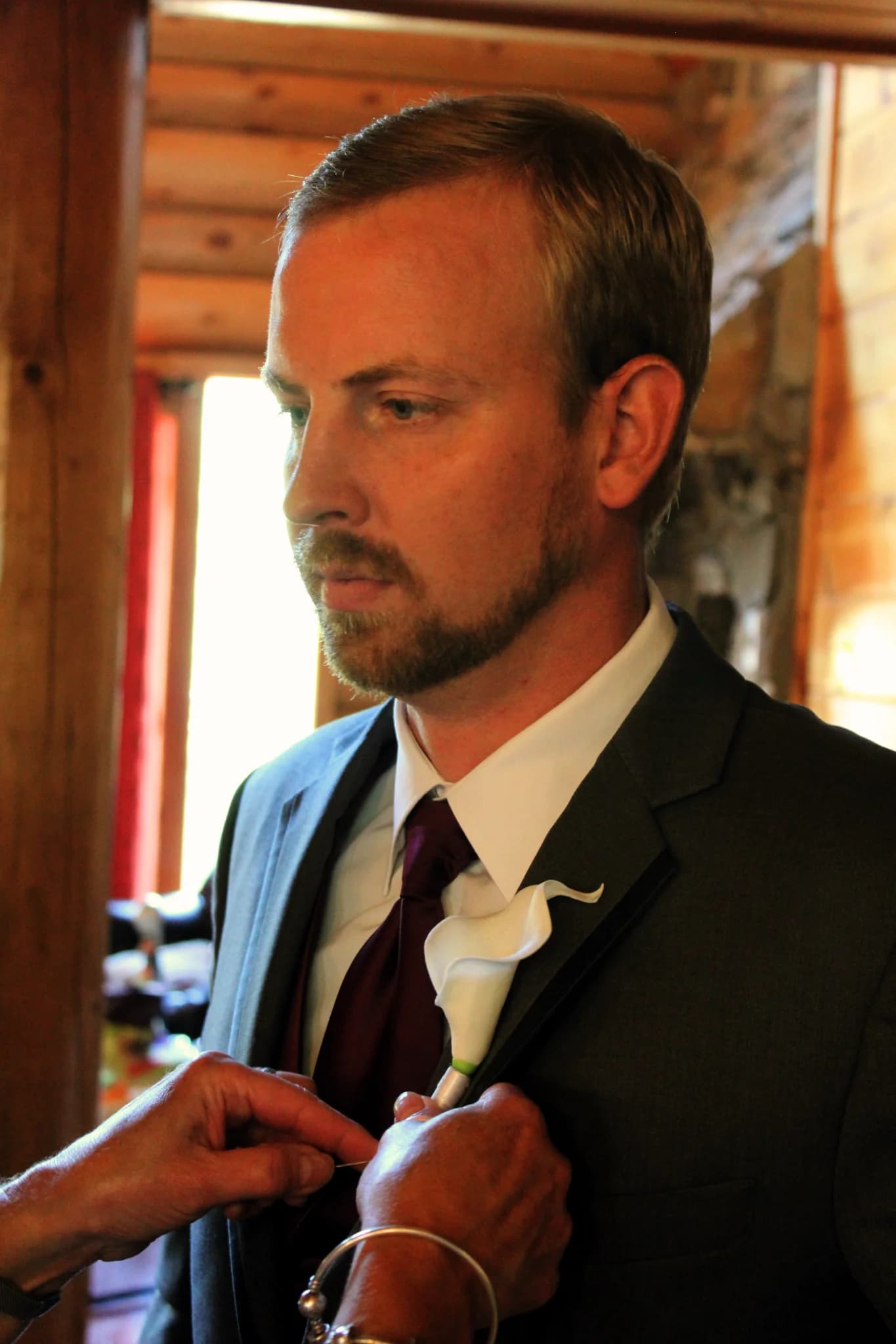 Groom in gray suit having a white boutonniere pinned on in rustic cabin at Moose Hollow Lodge in Pigeon Forge