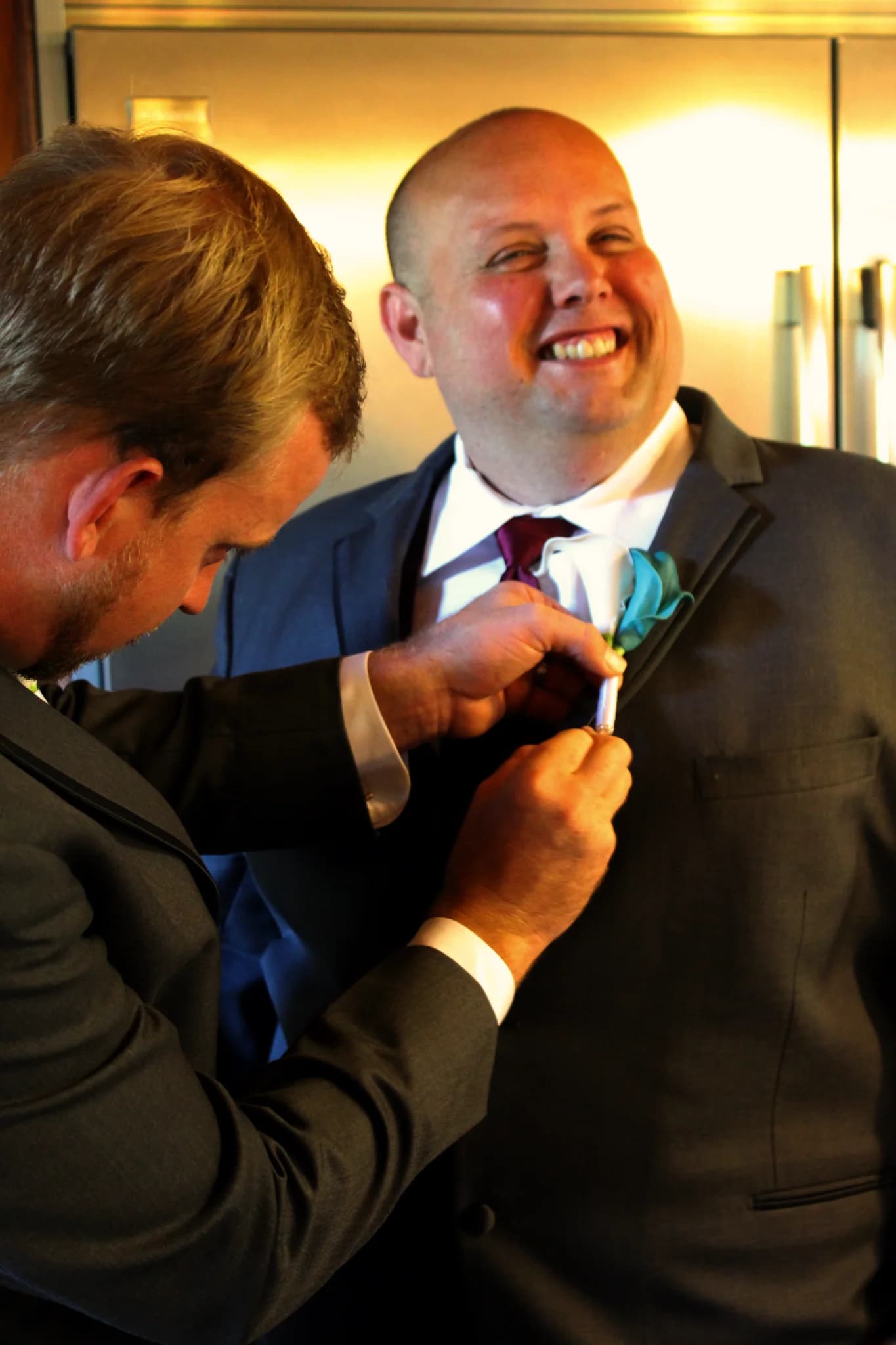 Smiling groom getting teal boutonniere pinned to grey suit at Moose Hollow Lodge in Pigeon Forge