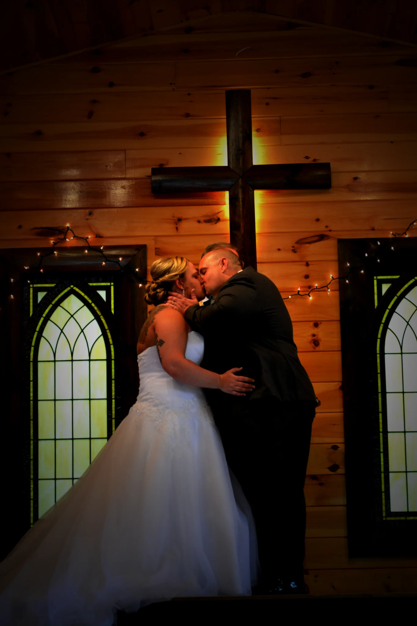 Newlyweds kissing in rustic chapel with wooden cross and stained glass at Moose Hollow Lodge in Pigeon Forge