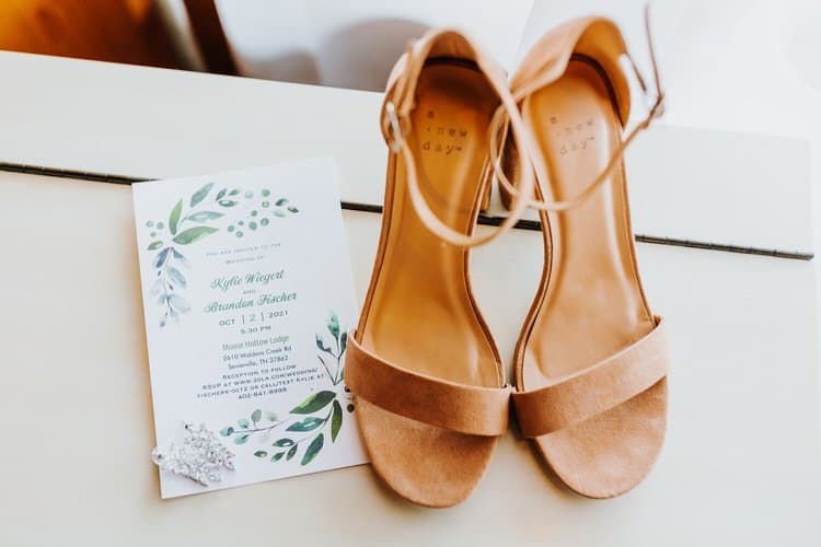 Wedding invitation for Kylie and Brandon, tan sandals, and a sparkly hair clip on a table at Moose Hollow...