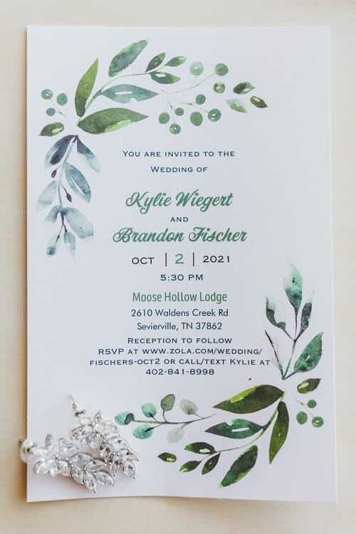 Wedding invitation for Kylie and Brandon at Moose Hollow Lodge, with silver leaf-shaped earrings.