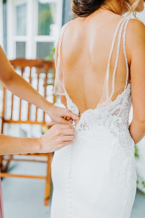 Hands buttoning the lace back of a white wedding dress. Interior shot at Moose Hollow Lodge, a luxury cabin venue.