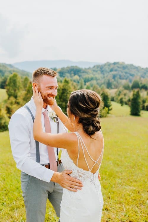 Wedding couple at Moose Hollow Lodge: woman in white dress, man in suspenders, standing in a grassy field with mountains.