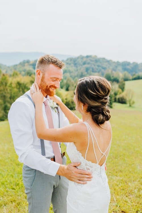 Bride in white dress and groom in white shirt and pink tie standing in a grassy field with rolling hills at Moose Hollow...