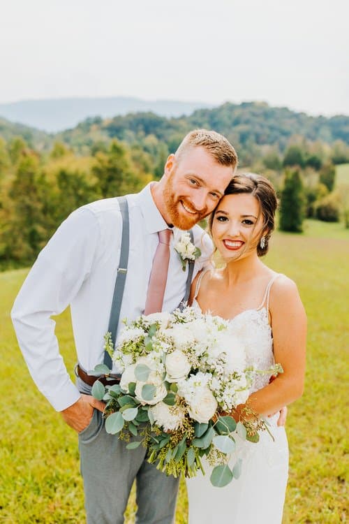 Wedding couple portrait outdoors in the Smoky Mountains. Groom wears suspenders, bride holds a white and green bouquet.