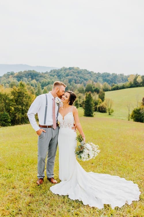 Wedding couple outdoors in a grassy field with Smoky Mountains in background, likely Moose Hollow Lodge.