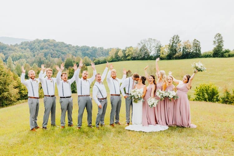 Wedding party of 14, bride, groom, 6 bridesmaids in dusty rose dresses, 6 groomsmen in grey, posing in a grassy field...