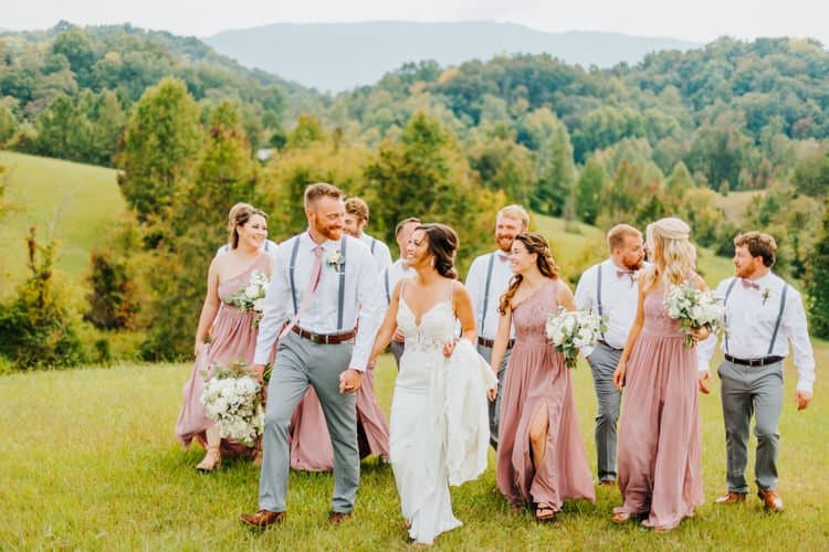 Wedding party walks on a grassy hill with Smoky Mountains in background at Moose Hollow Lodge, Sevierville.