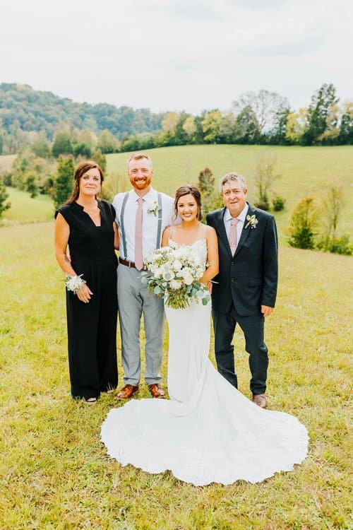 Bride in white dress with groom and two adults in a field. Hills and trees are visible in the background. Outdoor wedding...