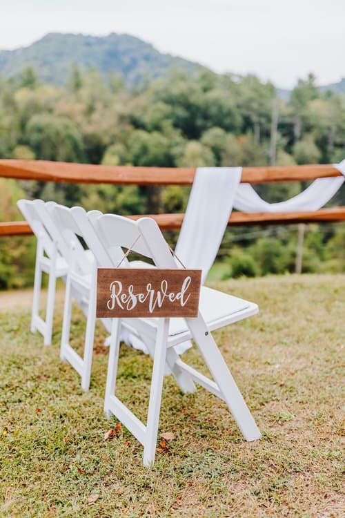White wedding chairs with a 'Reserved' sign and white fabric decor, wooden fence, and green mountains at Moose Hollow Lodge.
