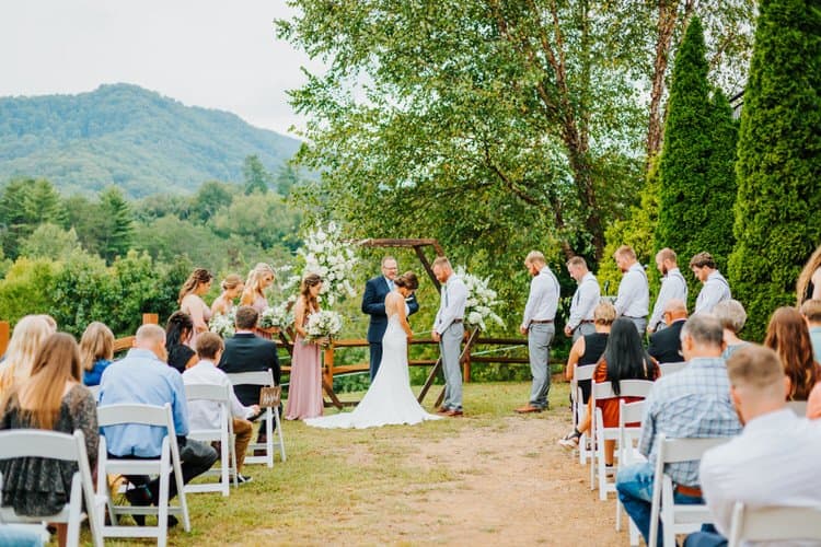 Outdoor wedding ceremony at Moose Hollow Lodge with a bride, groom, wedding party, guests, and mountain backdrop.