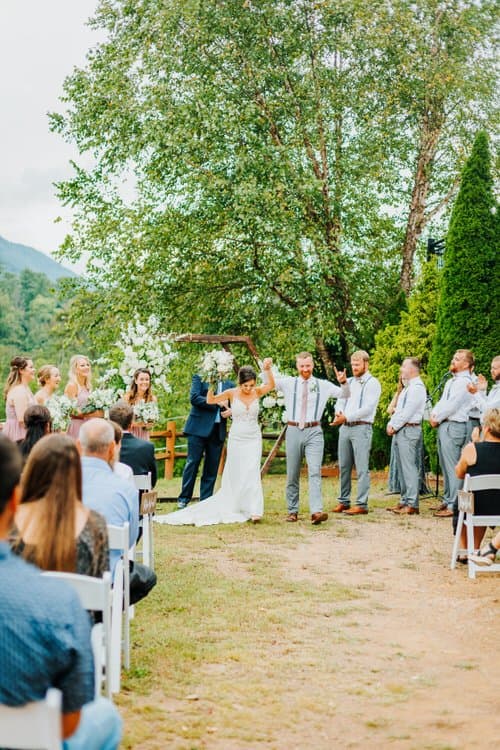 Wedding couple and party exiting an outdoor ceremony at Moose Hollow Lodge. Guests seated, mountains and trees visible.