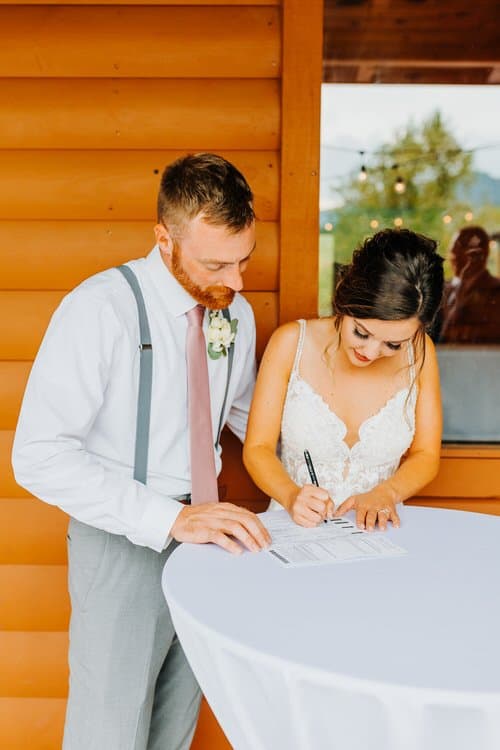 Couple signing marriage license on a white table outside a log cabin at Moose Hollow Lodge, Smoky Mountains.