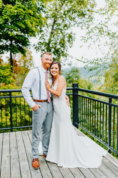 Man and woman in wedding attire on a deck overlooking trees and mountains at Moose Hollow Lodge.