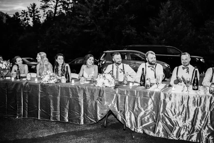 Outdoor wedding reception table with bride, groom, and guests. Champagne, flowers, and candles on the table. Night scene.