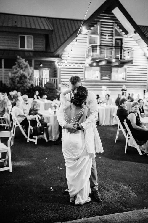 Couple dances outdoors at Moose Hollow Lodge with guests seated at tables under string lights. Black and white photograph.