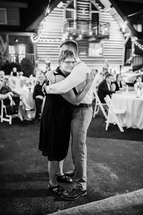 Black and white photo of a man and woman dancing outdoors at night. String lights and a log cabin, Moose Hollow Lodge,...