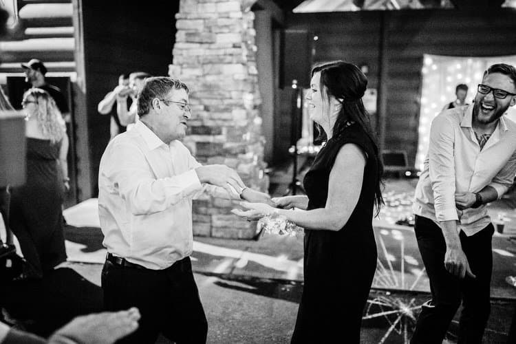 Guests dancing at a wedding reception. A man in a white shirt and a woman in a black dress interact while another guest...